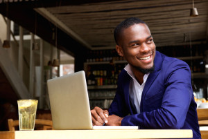 Smiling black businessman with laptop at cafe